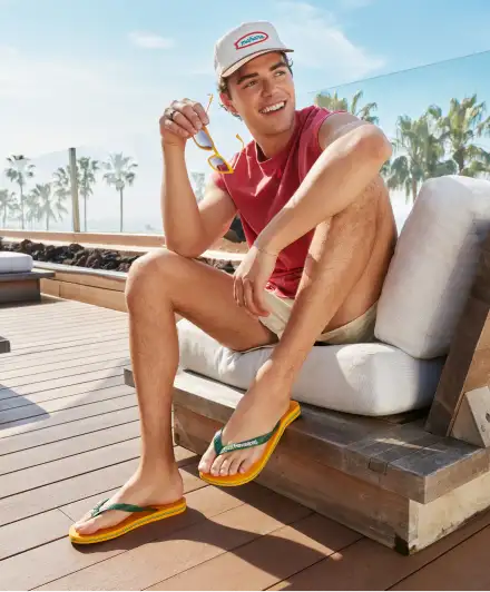 man walking in a park wearing a red hoodie, jean shorts, and black havaianas flip flops