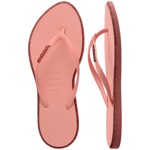 Pair of pink Havaianas flip flops with glitter accent and gold logo on the strap, with left shoe in focus, on a transparent background
