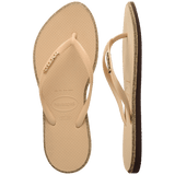 Pair of beige Havaianas flip flops with glitter accent and gold logo on the strap on a transparent background