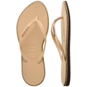 Pair of beige Havaianas flip flops with glitter accent and gold logo on the strap on a transparent background
