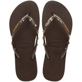 Pair of brown Havaianas flip flops with gold gems on the straps, on a white background
