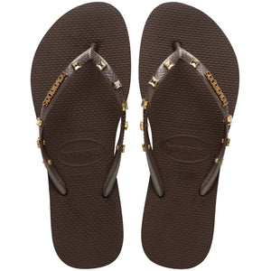 Pair of brown Havaianas flip flops with gold gems on the straps, on a white background