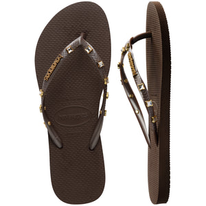 Pair of brown Havaianas flip flops with gold gems on the straps, on a white background with left shoe in focus