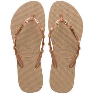 Pair of tan Havaianas flip flops with gold gems on the straps on a white background