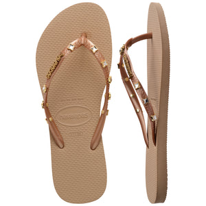 Pair of tan Havaianas flip flops with gold gems on the straps on a white background, with left shoe in focus