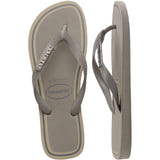 Havaianas Top Metropole flip-flop shown in top and side views. The sandal features light gray textured straps with metallic silver Havaianas logo accents, a light gray footbed, and an off-white sole with contrasting gray border stripes. The minimalist design offers a clean, modern look.