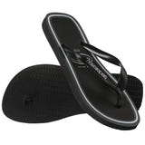 Havaianas Top Metropole flip-flop shown from an angled top and bottom view. The sandal features black textured straps with metallic silver Havaianas logo detailing, a black textured footbed, and a black sole accented with double white outline stripes around the perimeter. The black rubber outsole has a textured tread pattern for traction.