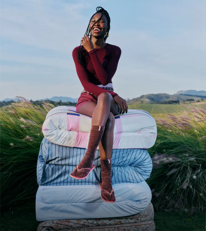 woman wearing socks with Havaianas flip flops sitting on a pile of mattresses in the middle of a grass field